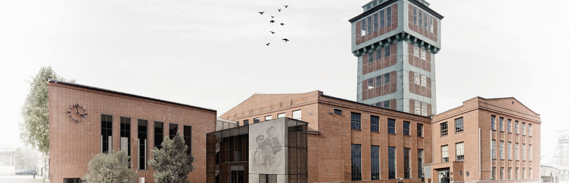 Das Bild zeigt eine Außenansicht eines Gebäudekomplexes aus roten Ziegeln mit einem markanten Turm in der Mitte. Links steht ein niedriges Gebäude mit einer großen Uhr an der Fassade. Auf dem Platz vor dem Gebäude laufen Menschen, einige betrachten den Eingangsbereich. Vögel fliegen über den hellen Himmel, und die Umgebung wirkt ruhig und aufgeräumt.