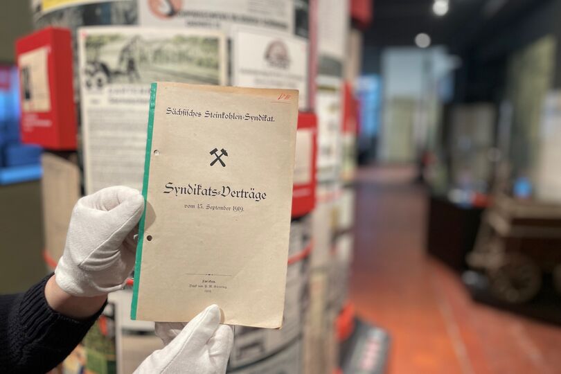 Abgebildet ist ein schmales Heft. Es ist ca. DIN A5 groß. Am linken Rand ist ein schmaler Streifen. Auf dem Heft steht „Sächsisches Steinkohlen-Syndikat.“ Darunter sind die Bergmannsinsignien „Schlägel und Eisen“ abgebildet.  Unter diesem befindet sich der Schriftzug „Syndikats-Verträge vom 15. September 1919“. Oben rechts ist die Zahl acht in römischen Ziffern handschriftlich geschrieben. Unten in der Mitte befinden sich noch folgende Hinweise „Zwickau/Druck P. M. Goering/1919.“